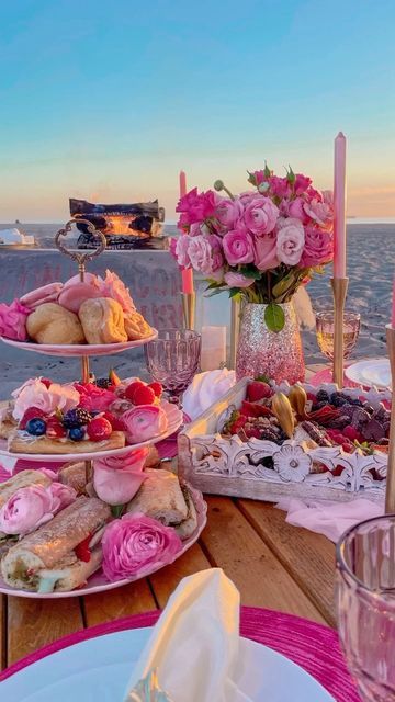 the table is set with pink flowers and desserts on it, overlooking the ocean