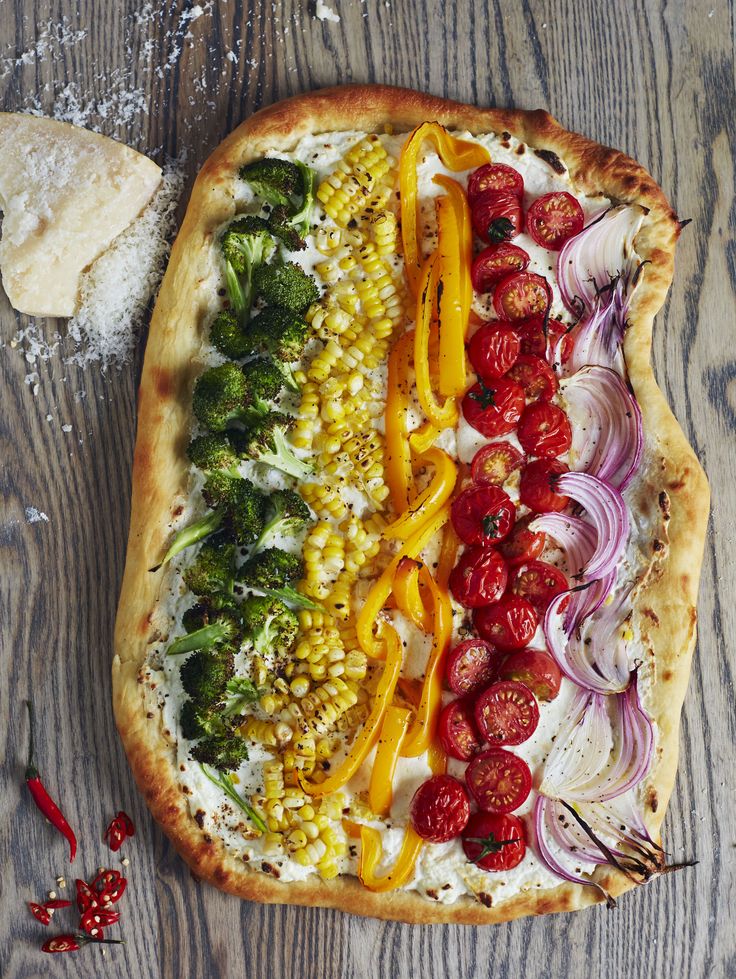 an uncooked pizza with tomatoes, corn and broccoli on it sitting on a wooden table