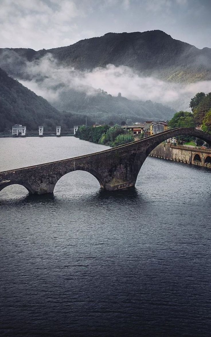 an old stone bridge spanning the width of a body of water with mountains in the background