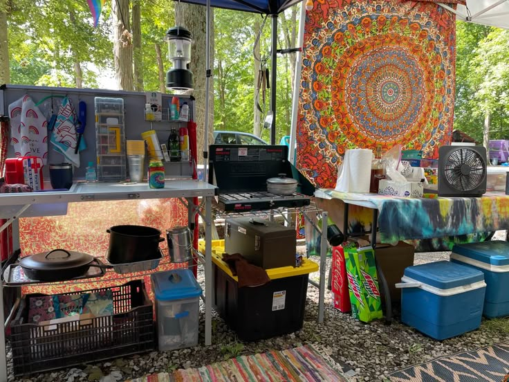 an outdoor area with various items on the table and in front of it is a colorful tapestry