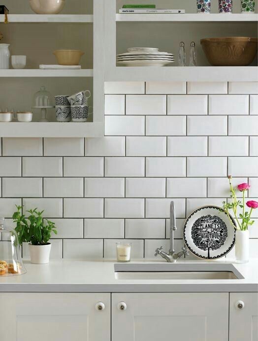 a kitchen with white subway tile and green plants on the counter top in front of it