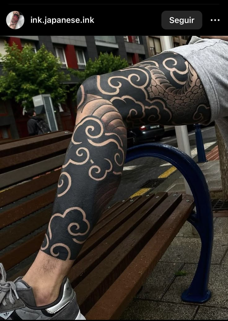 a man is sitting on a bench with his leg covered in black and white tattoos