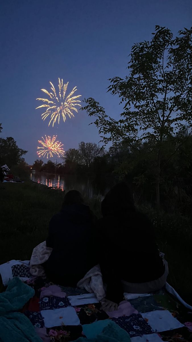 two people sitting on a blanket watching fireworks