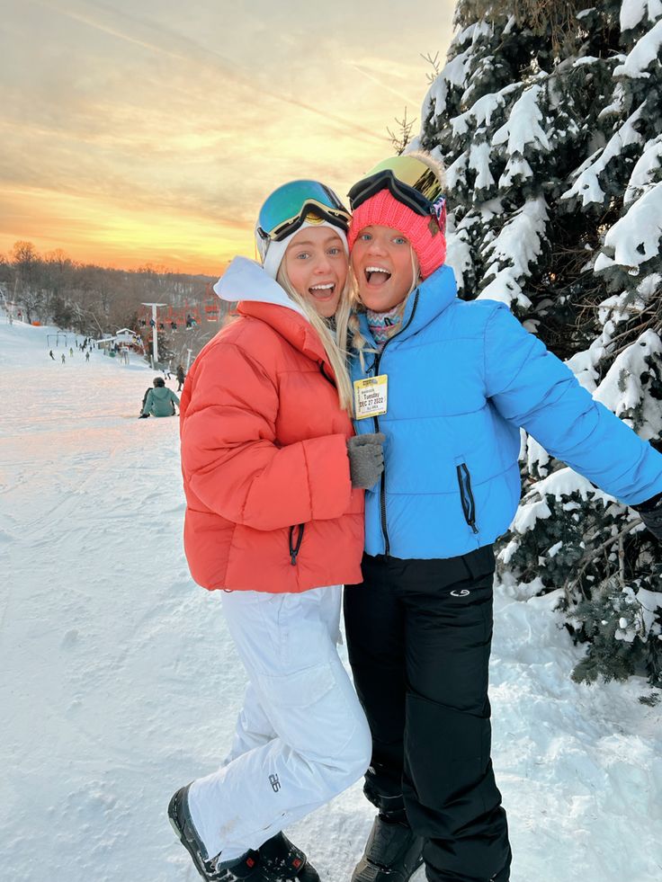 two people standing next to each other in front of a tree on a ski slope