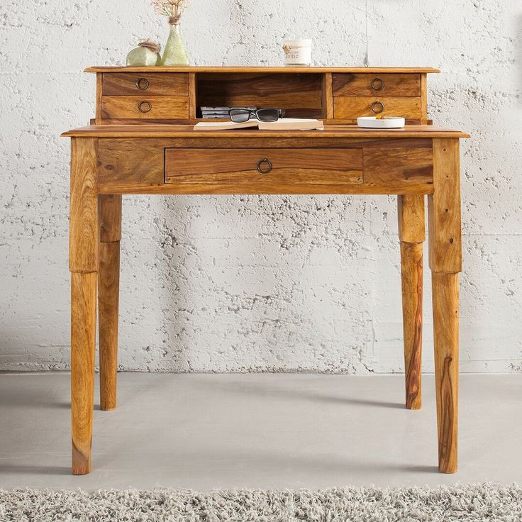 a small wooden desk sitting in front of a white wall with a vase on it