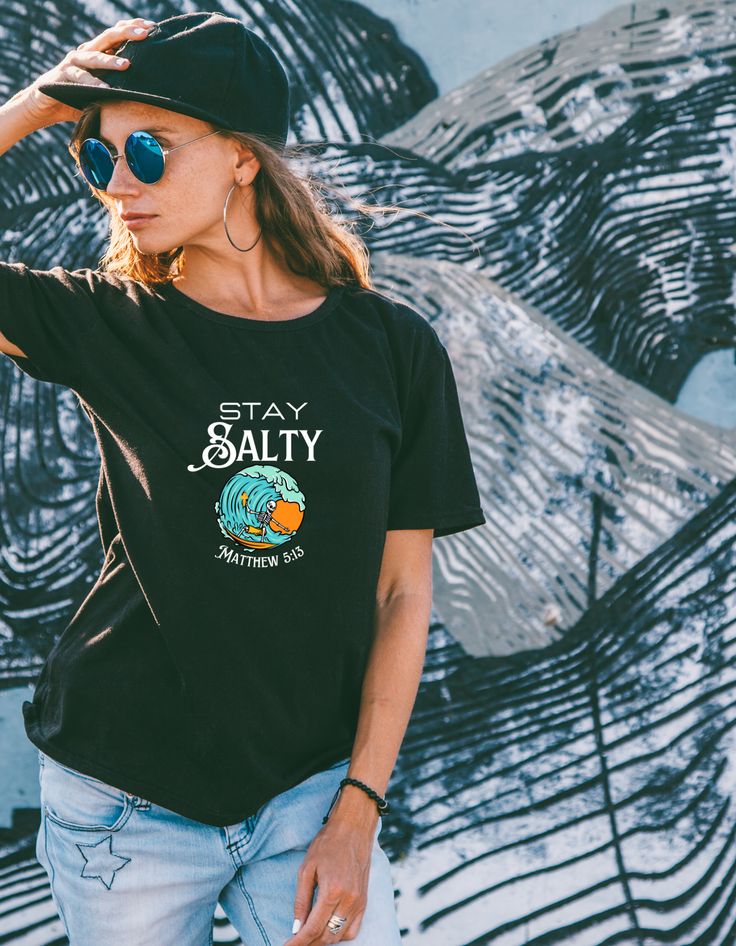 Unleash your inner surfer with this eco-friendly t-shirt that showcases a skeleton shredding a wave and clutching a cross. Plus, for a biblical twist, we tucked in Matthew 5:13 at the bottom of the wave. This one-of-a-kind design was a custom ask and it came out just right! Our Re-Tee is crafted from 100% recycled fabric, never dyed again, using rescued materials that would have wound up in the junkyard. Soft. Cozy. Top-notch. When you're doing good for Mother Earth, it's a good feeling for your Casual Black T-shirt For Surfing, Black Graphic Tee For Surfing, Black Letter Print T-shirt For Surfing, Black Surfing T-shirt With Letter Print, Black Screen Print Surfing T-shirt, Black Graphic Print T-shirt For Surfing, Cotton T-shirt For Surfing Vacation, Relaxed Fit Crew Neck Surfing T-shirt, Black Surfing T-shirt With Screen Print