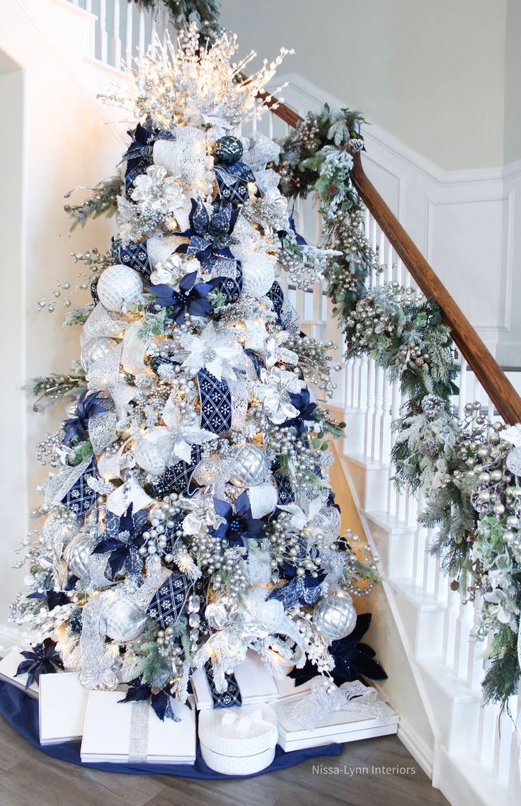 a white christmas tree with blue and silver decorations on it's bottom tiers