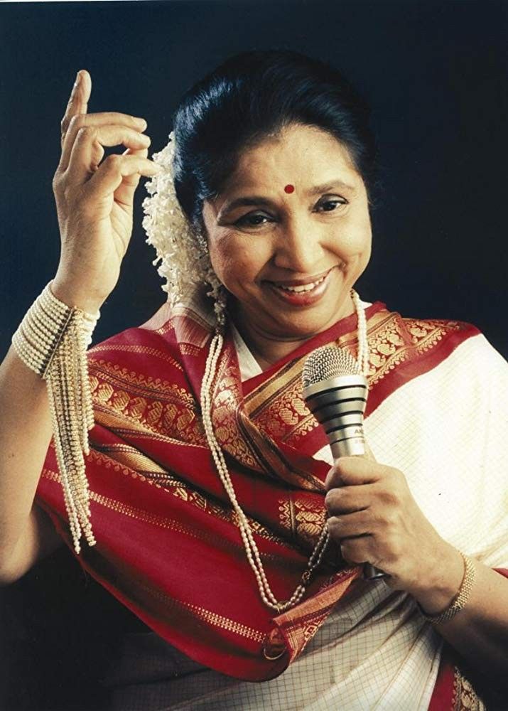 a woman holding a microphone in her right hand and wearing a sari on the other