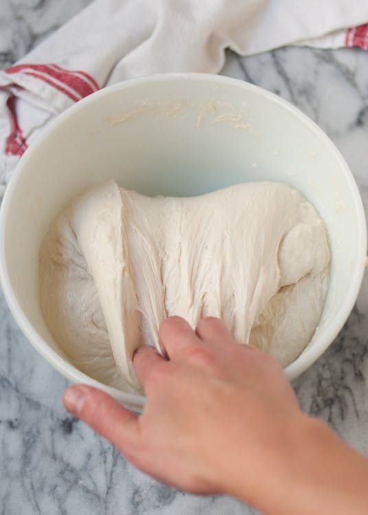 someone is mixing dough in a bowl on the counter top with their hand over it