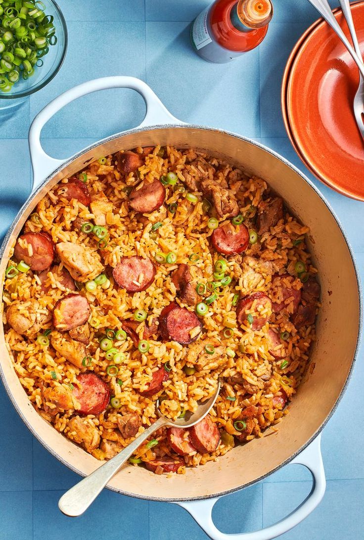 a pan filled with rice and sausage on top of a blue tablecloth next to bowls of peas