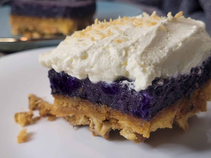 a piece of cake on a white plate with blueberries and whipped cream frosting