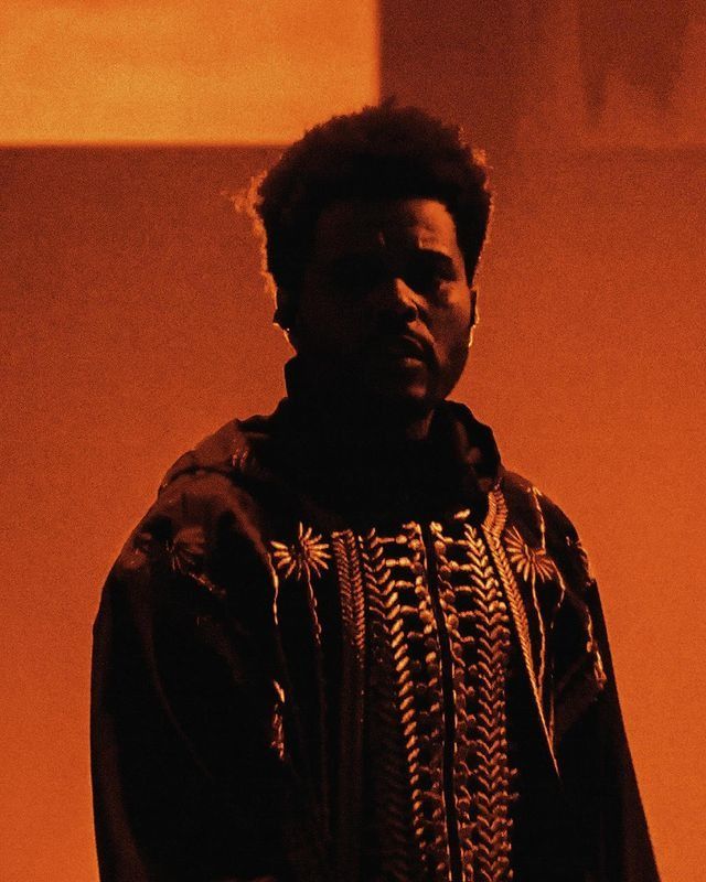 a man with an afro standing in front of a red wall and looking at the camera