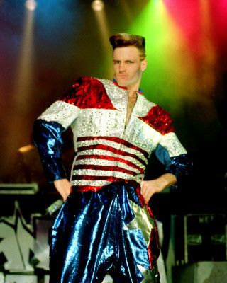 a man dressed in an american flag outfit standing on stage with his hands on his hips