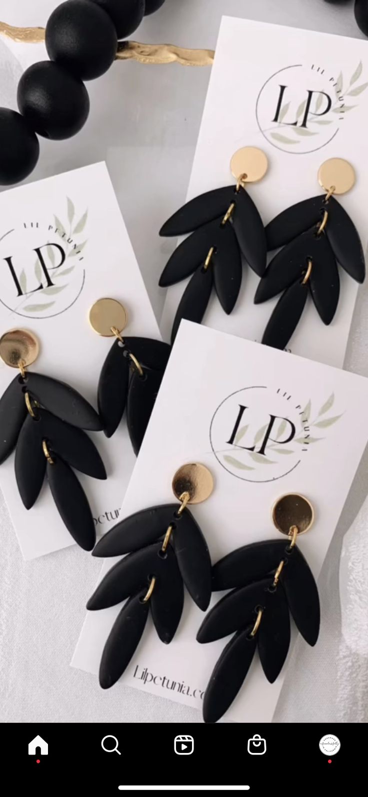 two pairs of black and gold earrings on top of a white card next to beads