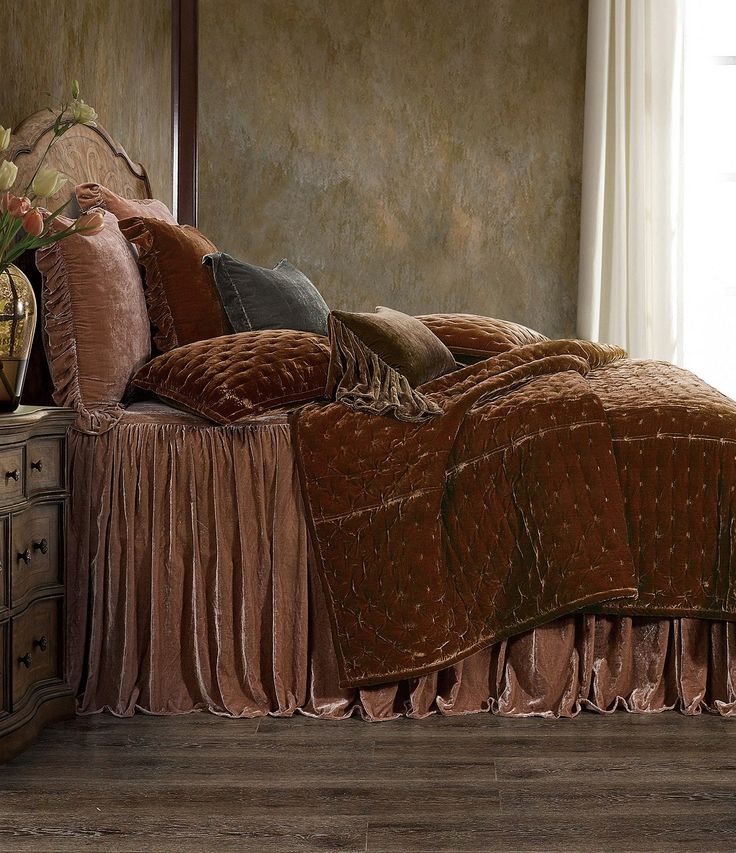 a bed with a brown bedspread and pillows on top of it next to a window