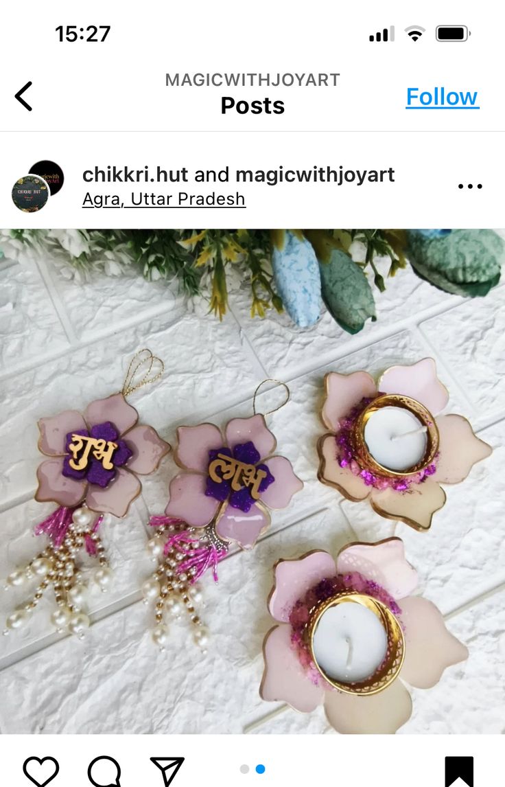 three pink and gold flower shaped candles on top of a white table with flowers in the background