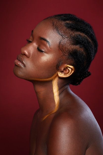 a woman with her eyes closed wearing gold ear rings and braids, against a red background