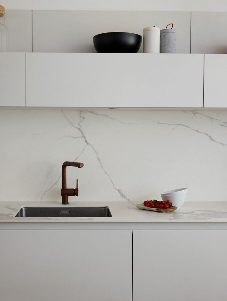 a kitchen with white cabinets and marble countertops, including a sink that has a faucet