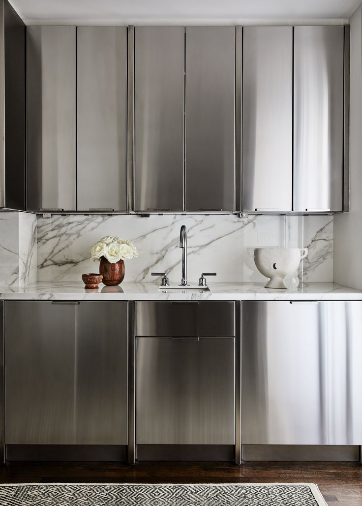 a kitchen with stainless steel cabinets and white marble counter tops, along with a rug on the floor