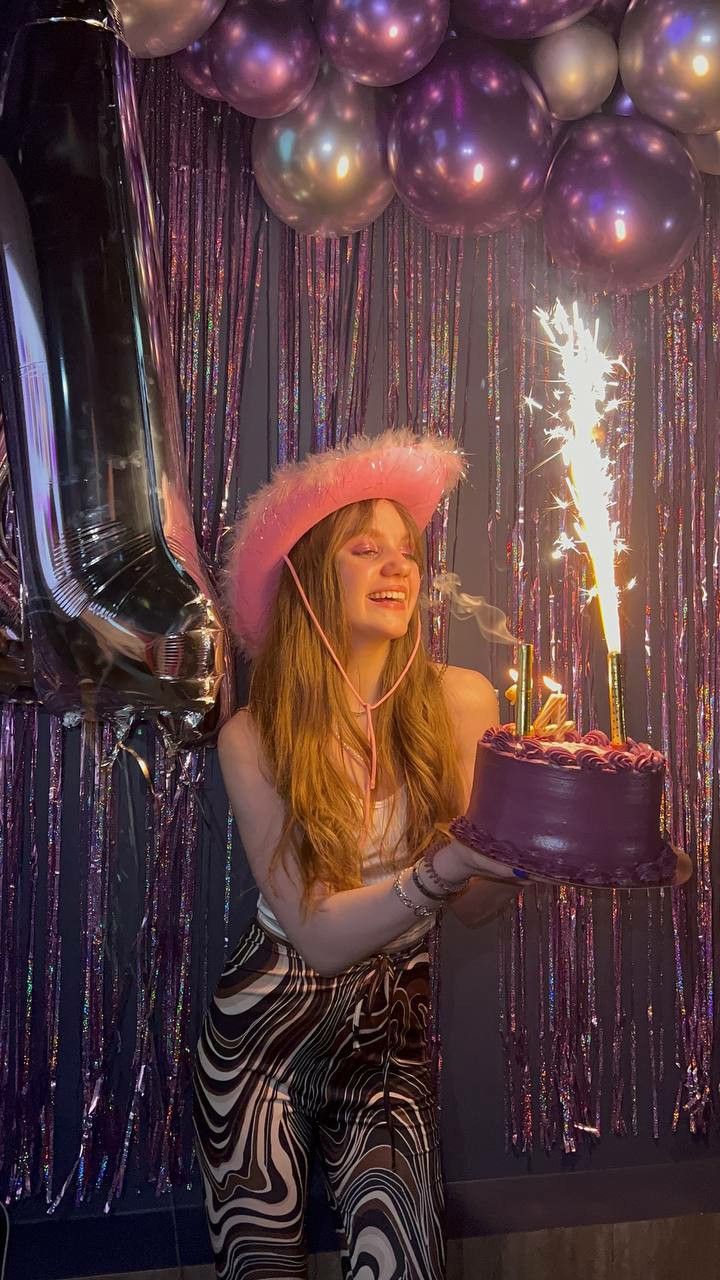 a woman holding a birthday cake with sparklers on it in front of balloons and streamers