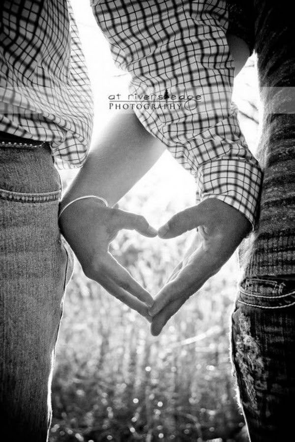 two people holding hands making a heart shape with their hands while standing in the grass