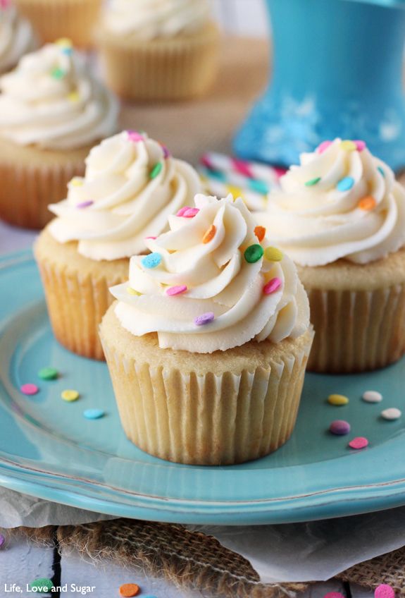 three cupcakes with white frosting and sprinkles on a blue plate