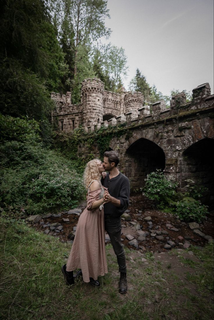 a man and woman standing next to each other in front of an old stone bridge