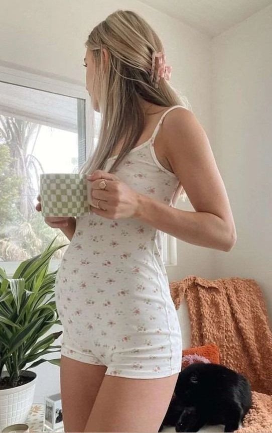 a woman standing in front of a window holding a cup and looking at her cat