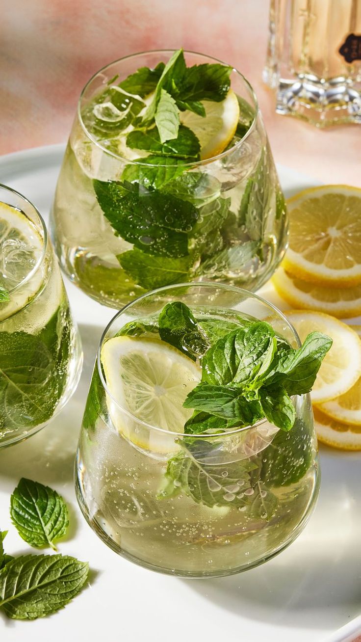 three glasses filled with lemonade and mint tea on a white plate next to sliced lemons