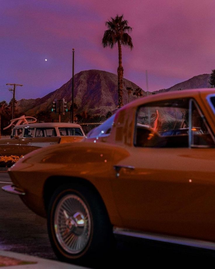 an orange car is parked on the side of the road in front of palm trees