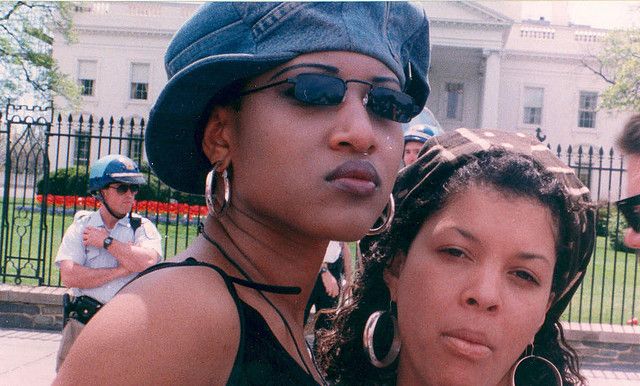 two women standing next to each other in front of a white house with police officers