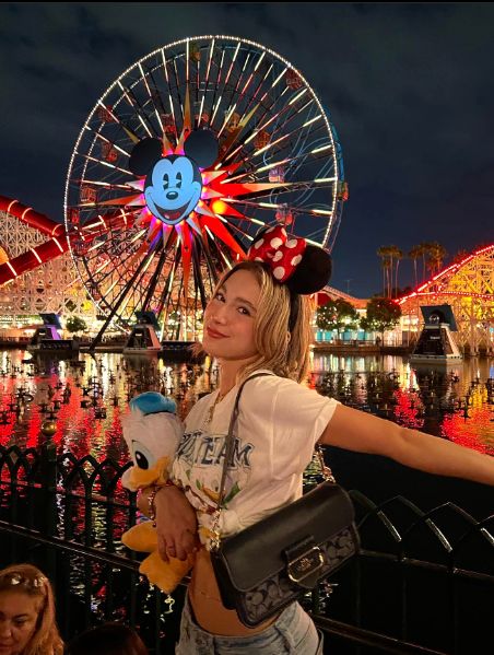 a woman standing in front of a ferris wheel with a mickey mouse on her head