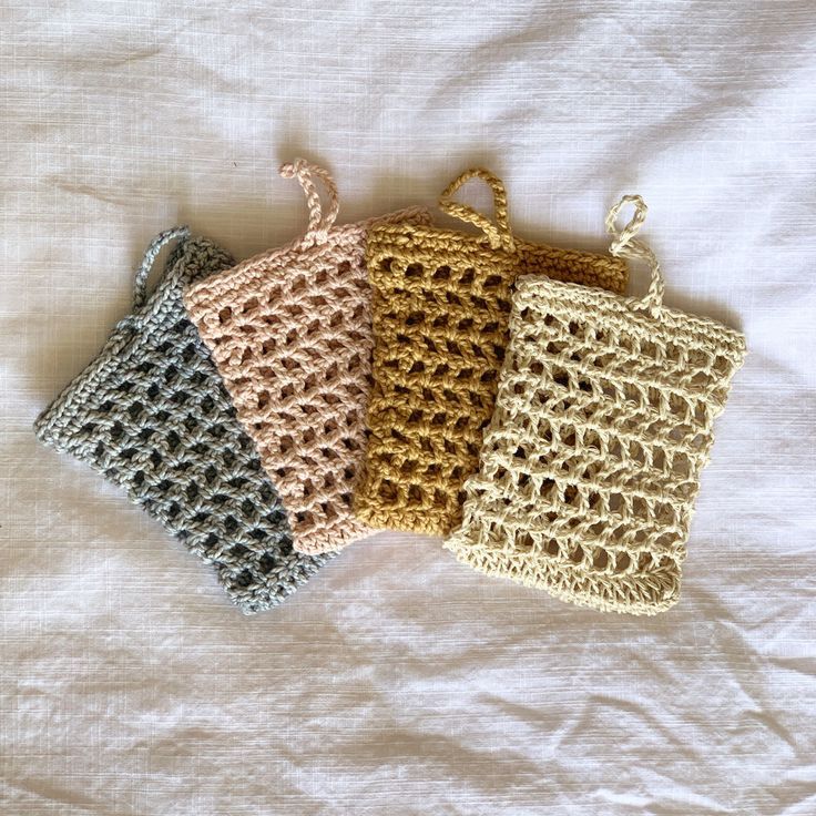 four crocheted purses sitting on top of a white bed covered in sheets