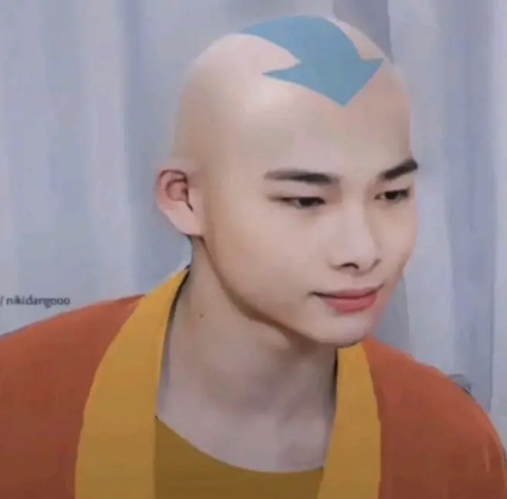 a bald man with blue arrows on his head and an orange shirt is looking at the camera