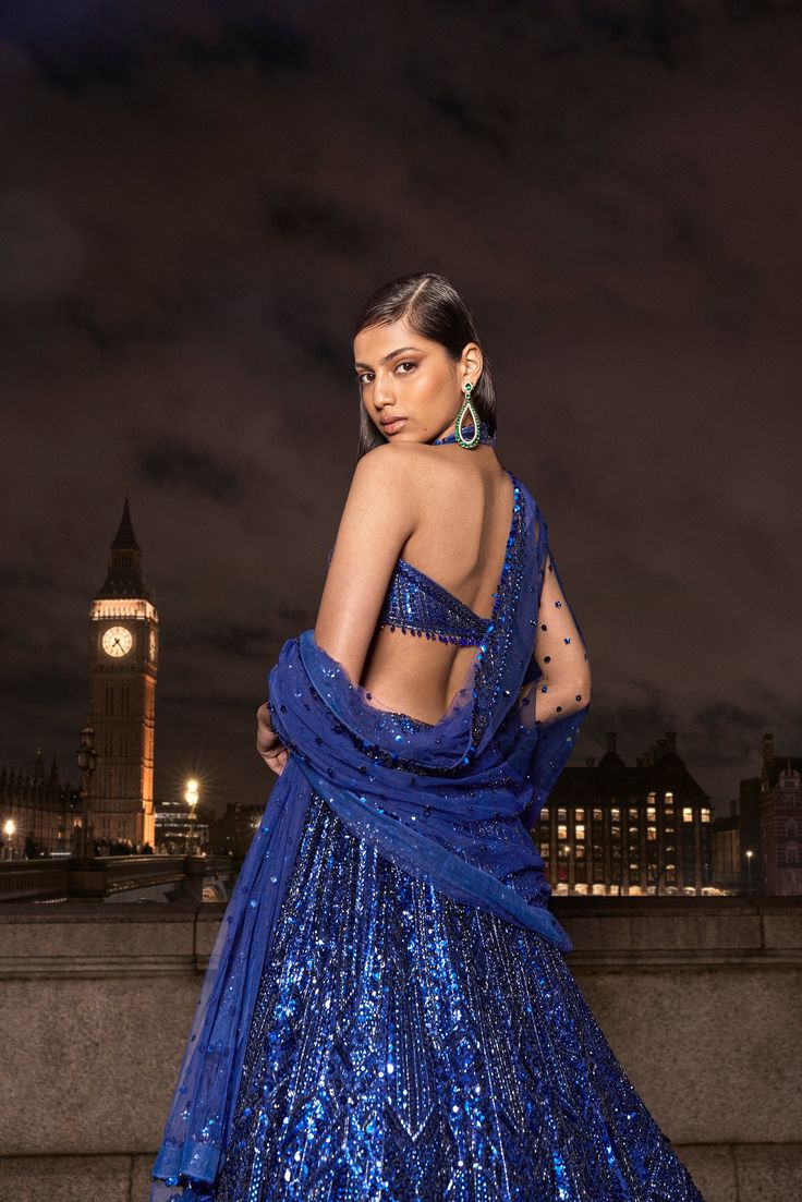 This navy lehenga set features all over tonal sequin embroidery in a geometric pattern. The ensemble is paired with a strappy blouse with tassels at the waist and a matching net dupatta.From Seema Gujral's For the love of London collection. DELIVERY TIMEPlease allow 8-12 weeks for your outfit to arrive. FABRIC DETAILSNet Professional cleaning only. Blue Glamorous Lehenga For Reception, Glamorous Blue Festive Lehenga, Glamorous Blue Lehenga For Festive Occasions, Glamorous Blue Lehenga With Zari Work, Blue Sequined Sets For Reception, Glamorous Blue Sets For Reception, Blue Sequined Party Wear Sets, Glamorous Blue Sequined Lehenga, Blue Sequin Sets For Diwali