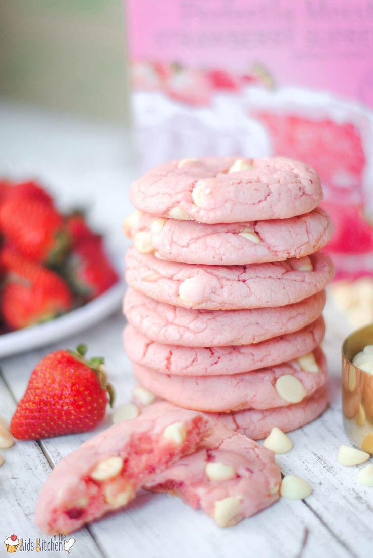 a stack of pink cookies next to some strawberries on a white table with other food items in the background