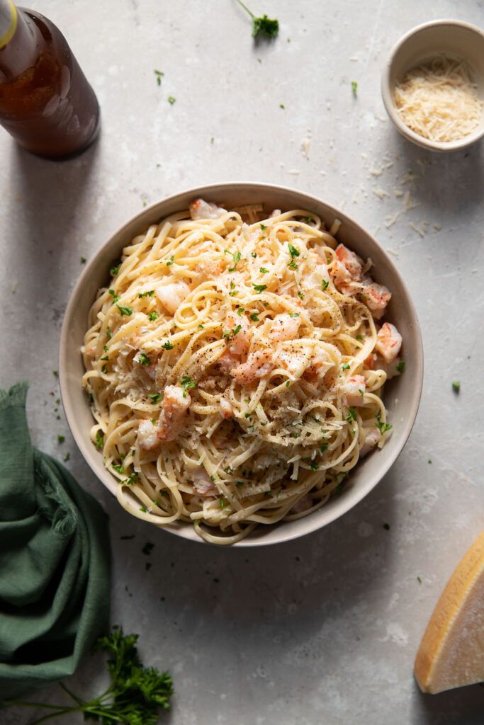 a bowl of pasta with shrimp and parsley on the side next to two slices of bread