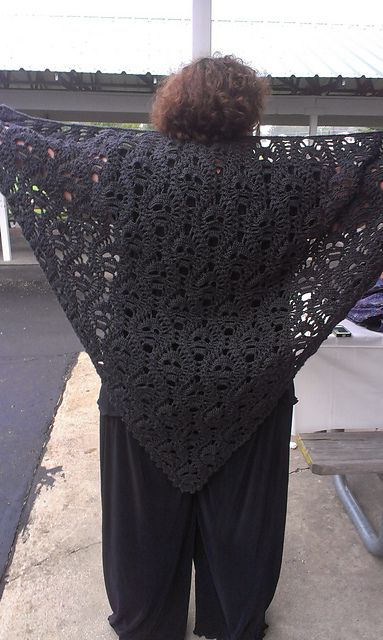 a woman standing on the sidewalk wearing a black crocheted shawl over her shoulders