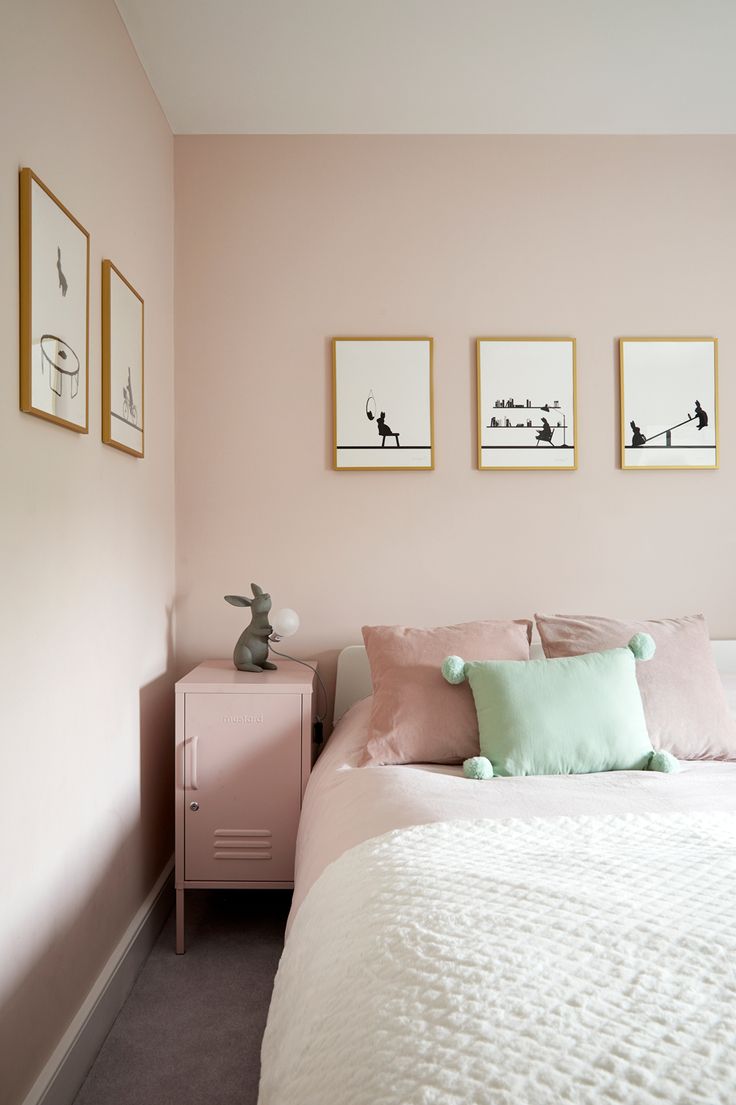 a bedroom with pink walls and pictures on the wall above the bed, along with two nightstands