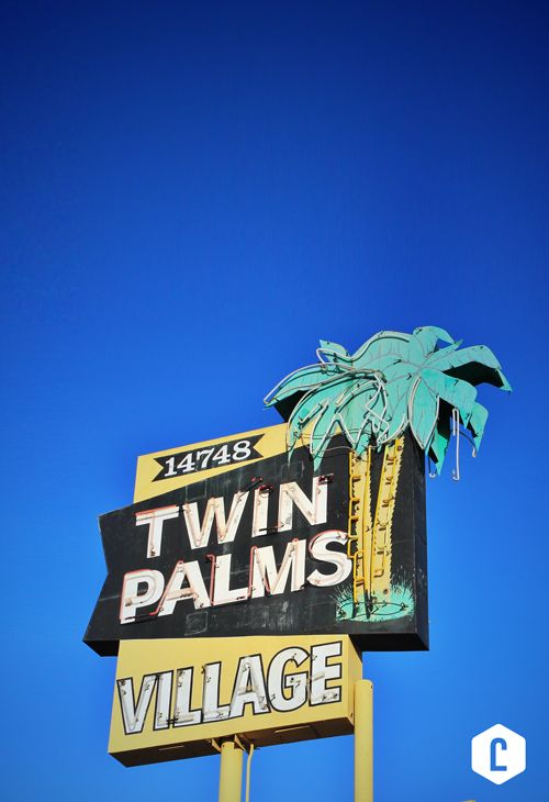 a sign for twin palms village in front of a blue sky