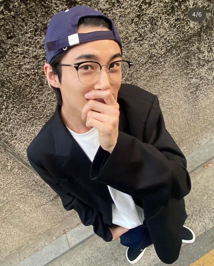 a young man wearing glasses and a cap is posing for the camera with his hand under his chin