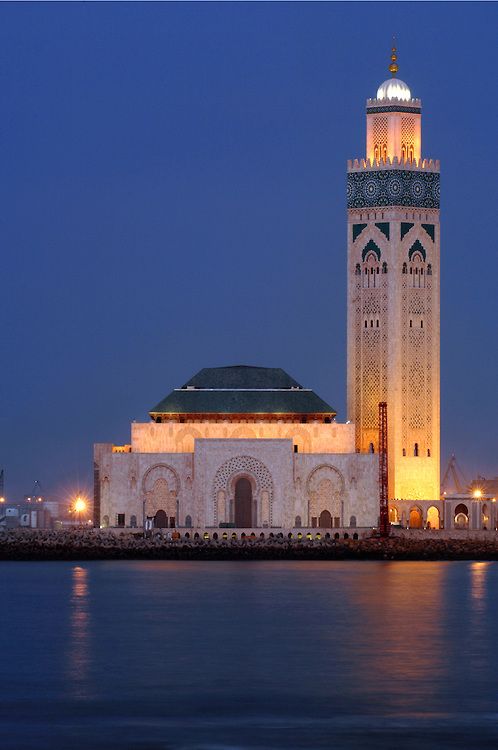 a tall white building sitting on top of a lake next to a city at night