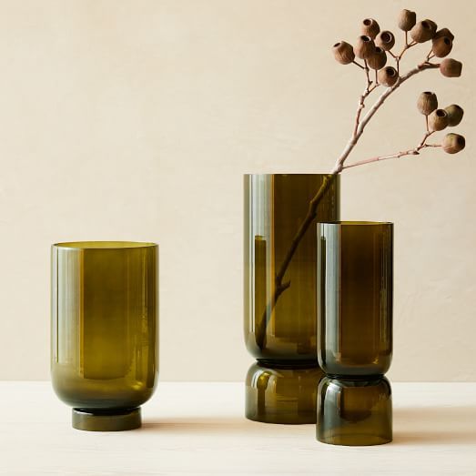 two green vases with a single candle in one and a small plant in the other