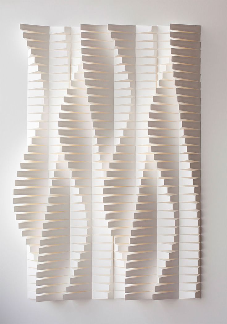 an art piece made out of white paper with wavy lines on the wall behind it