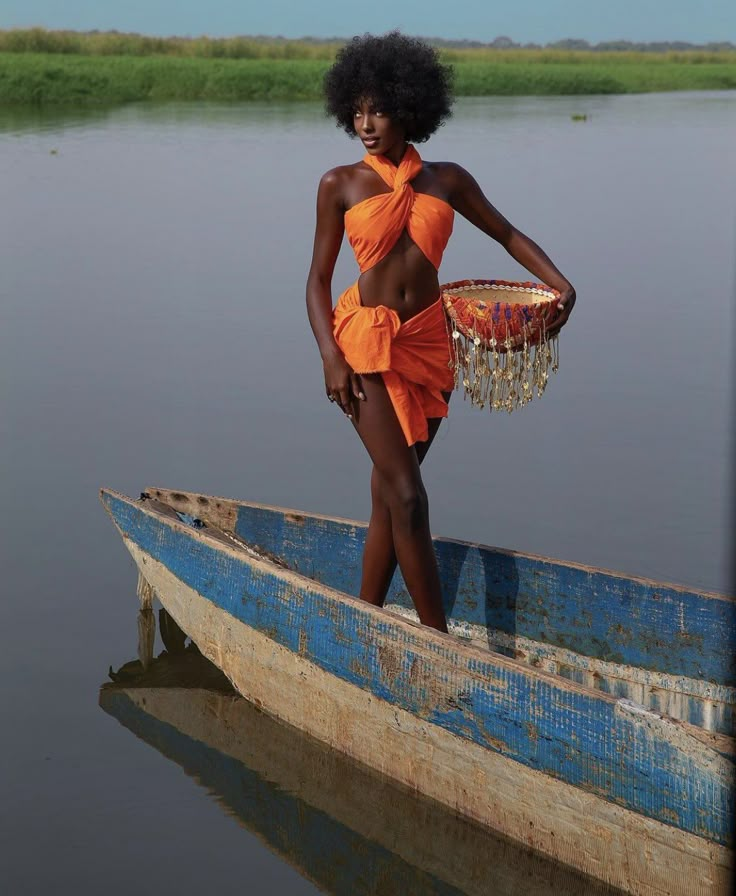 a woman in an orange dress is standing on a small boat with a basket hanging from it