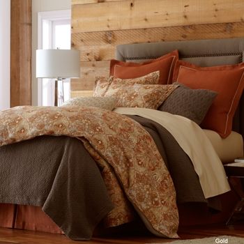 a bed with brown and tan comforters in a bedroom next to a chair, table and lamp