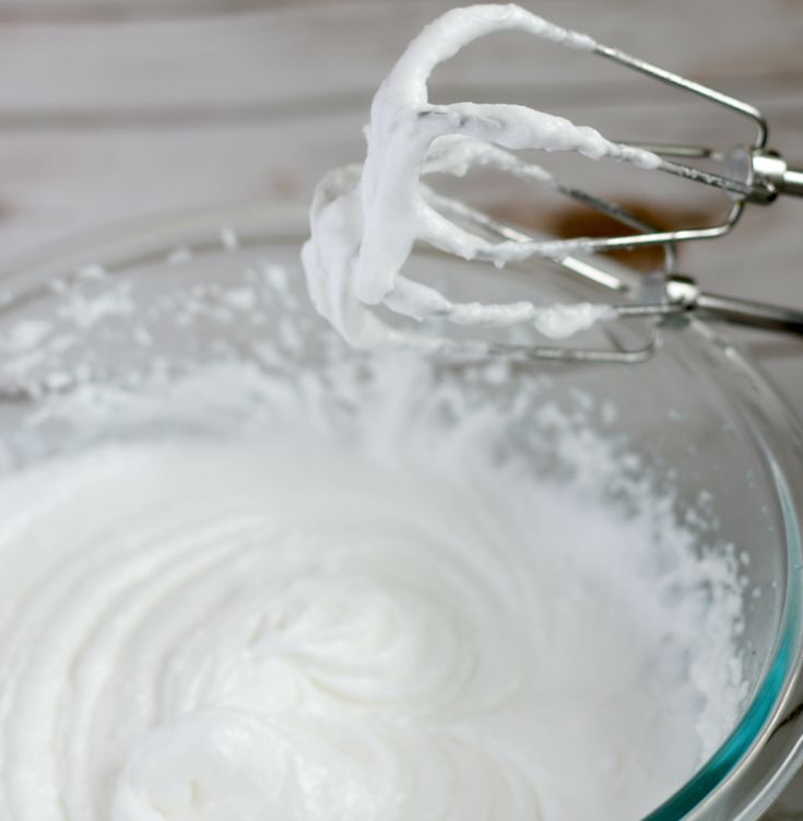 a bowl filled with whipped cream on top of a wooden table next to a whisk