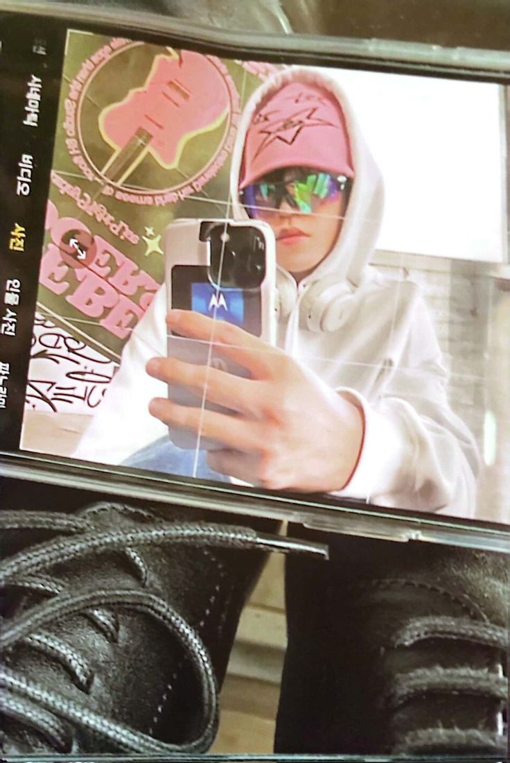 a person taking a selfie with their cell phone while wearing black shoes and hoodie