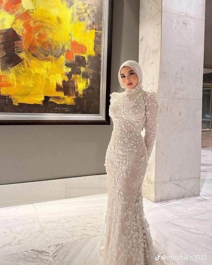 a woman standing in front of a painting wearing a white hijab and head scarf