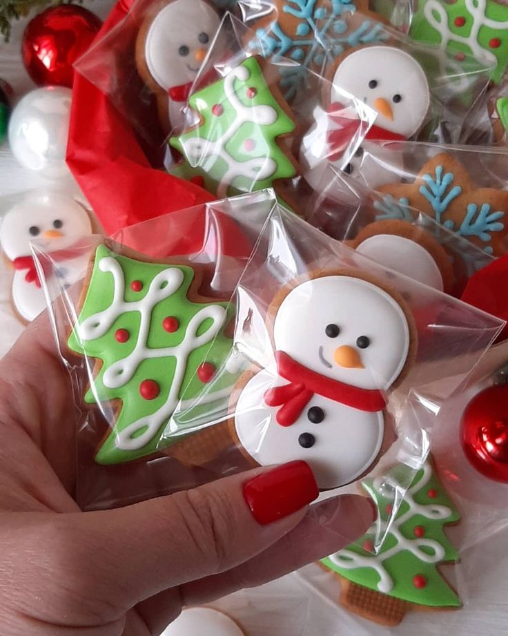 a hand is holding some decorated cookies in the shape of christmas trees and snowmen